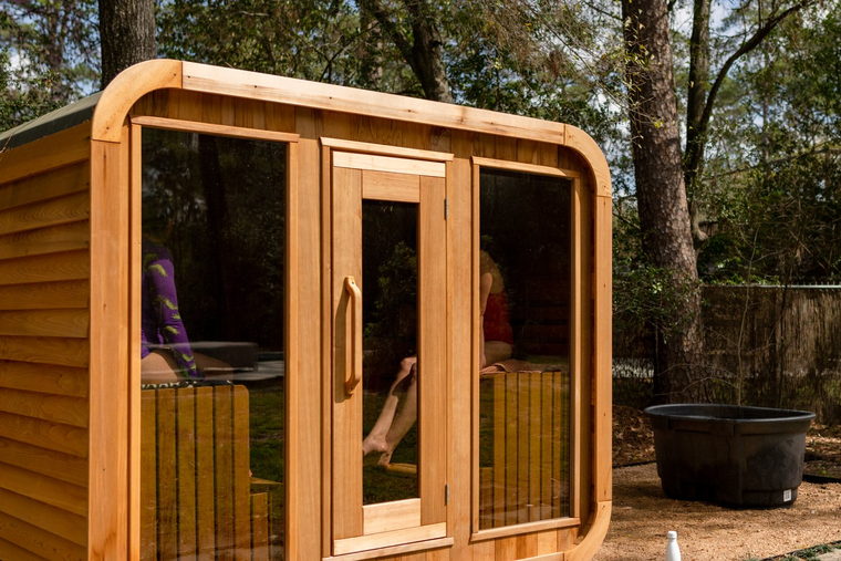 The cedar sauna in use, two people seated inside, with a cold plunge tub alongside it.